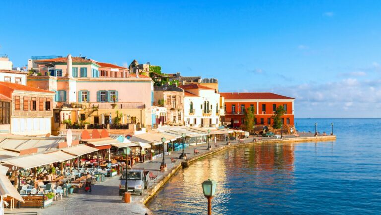 Hotels in Chania: Sunny waterfront in Chania, Crete with cafes and calm sea under a clear blue sky.