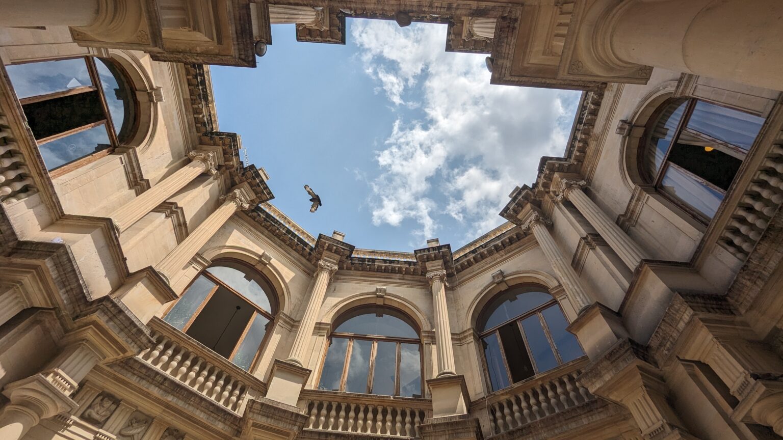 Looking up at the sky through the courtyard of Heraklion's Venetian Loggia with a bird flying overhead.